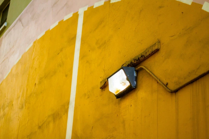 A security light mounted on a yellow wall.